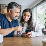 Genitore e figlio adolescente discutono di sicurezza digitale davanti a uno smartphone