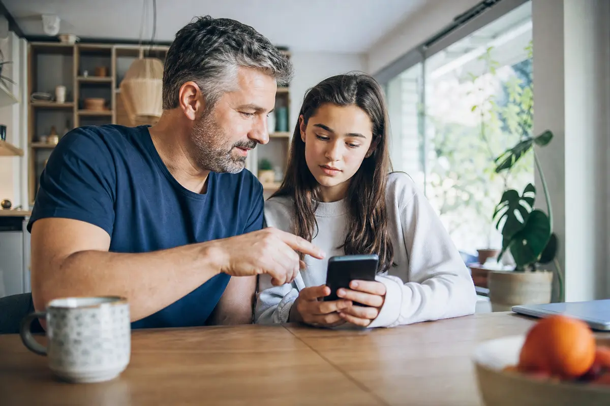 Genitore e figlio adolescente discutono di sicurezza digitale davanti a uno smartphone